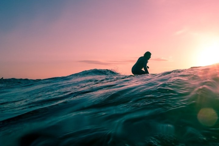 Surfer on a wave at sunset with a pink sky and sun on the horizon.