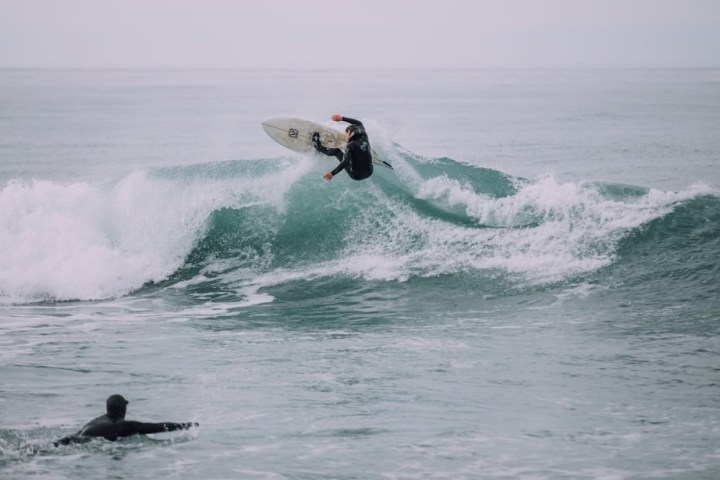 Surfer catching air on wave while another watches in the ocean.