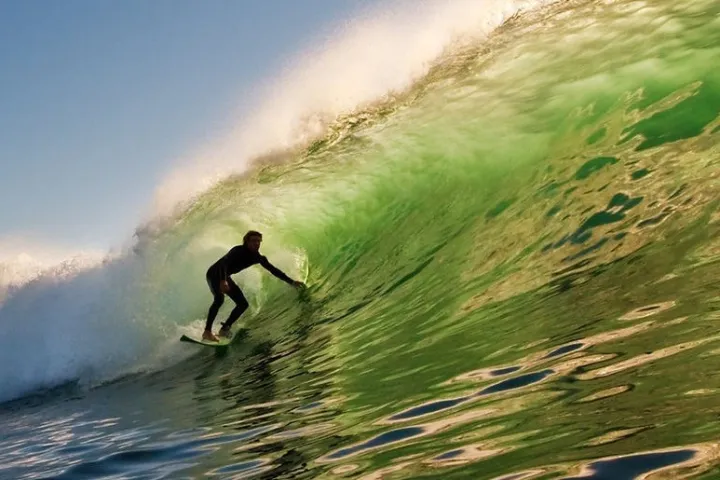 Surfer riding a large green wave under a clear blue sky.