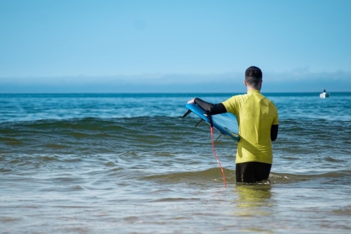 Person in yellow shirt holding a surfboard, standing in the ocean facing away.