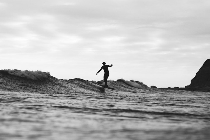 Silhouette of a surfer riding a wave in black and white, with cliffs in the background.