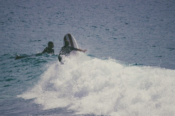 Two people surfing on waves in the ocean, with a surfboard visible.
