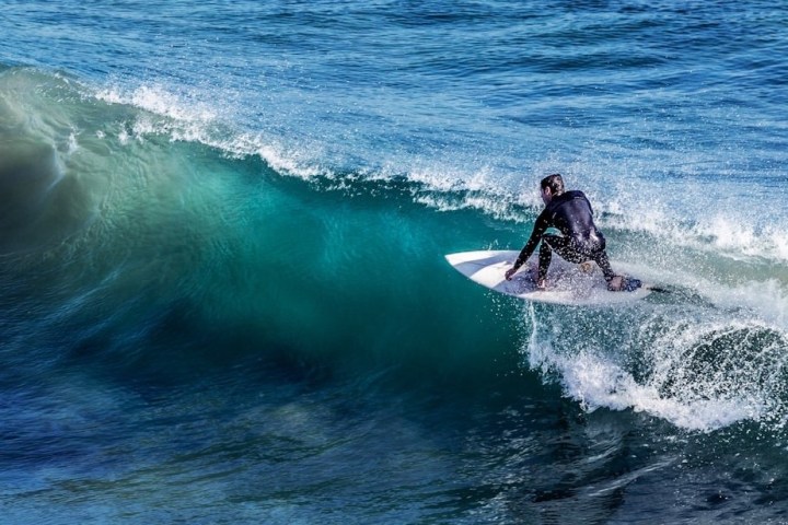 Surfer in a wetsuit riding a wave on a clear blue ocean.