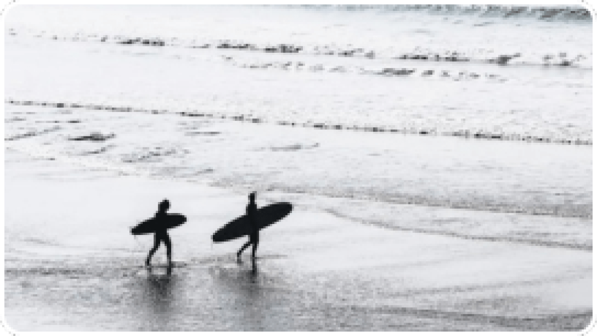 Two surfers walking on a beach with their surfboards, waves in the background.