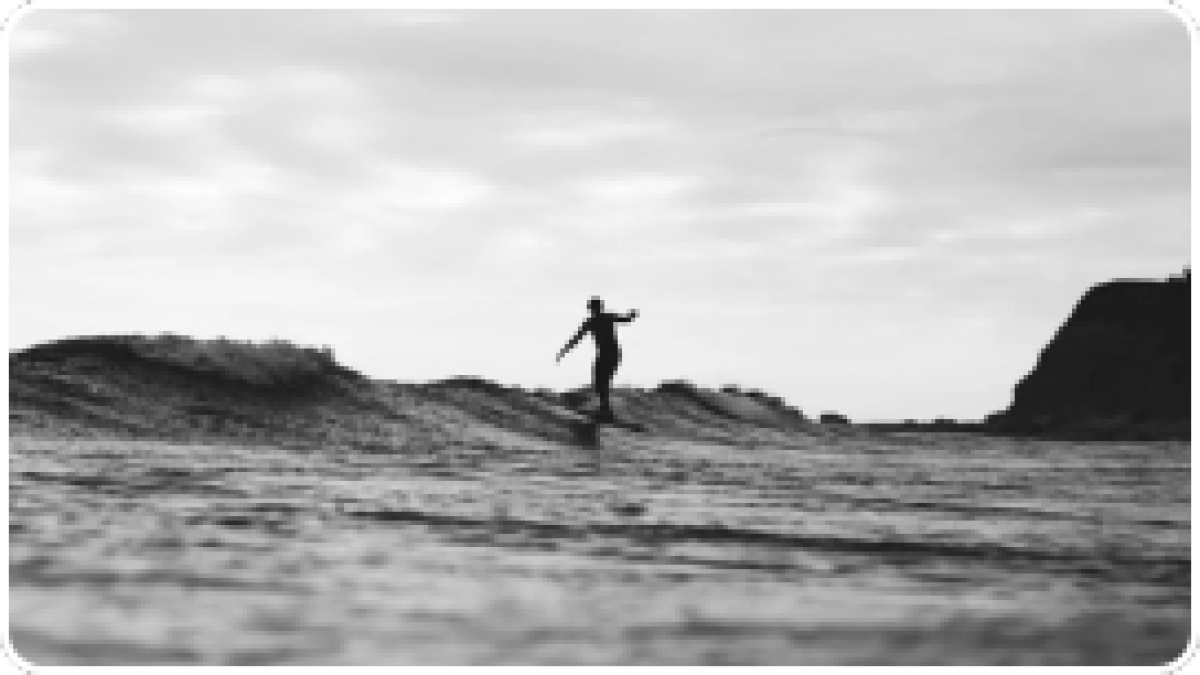 Silhouette of a surfer riding a wave in black and white.
