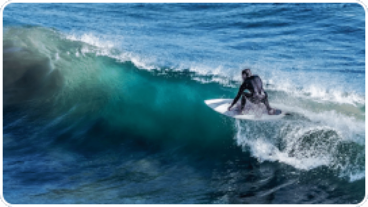Surfer riding a wave on a bright blue ocean, wearing a wetsuit.