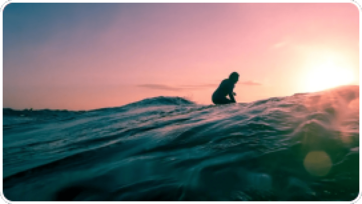 Silhouette of a person surfing on a wave at sunset with pink and purple sky.