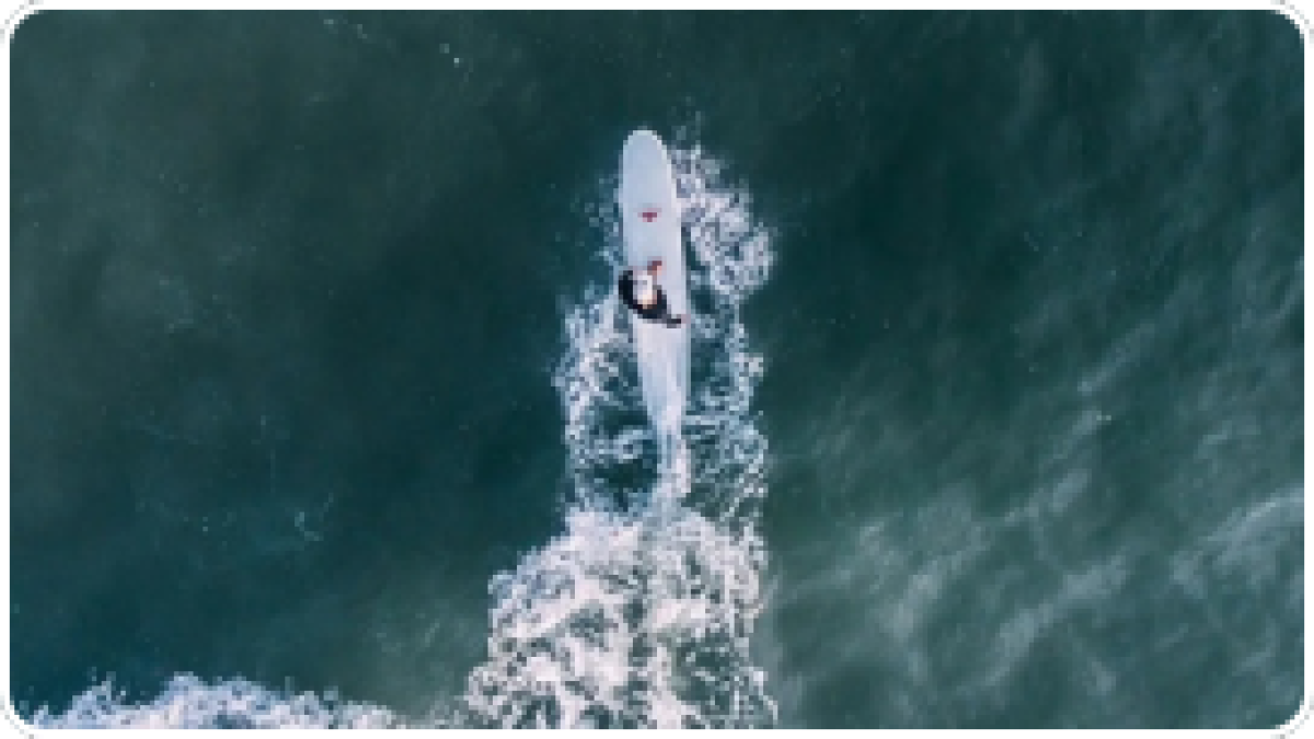 Aerial view of person paddleboarding on ocean waves, trailing a white wake.