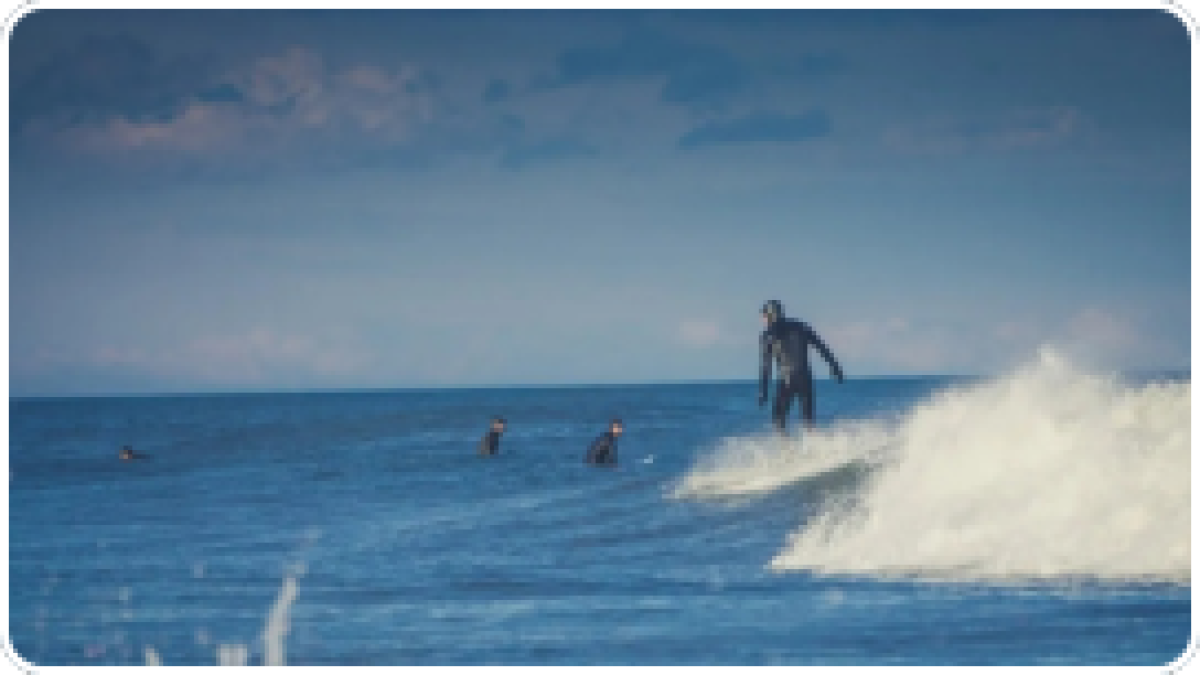 Surfer riding a wave with others waiting in the ocean.
