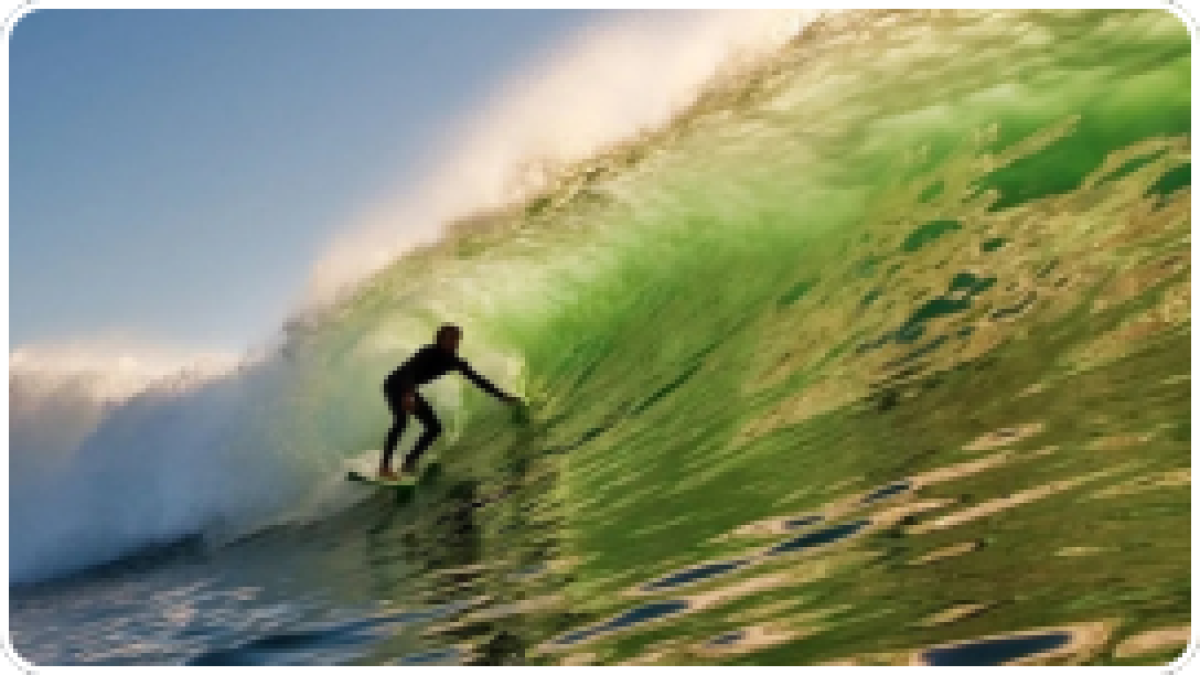 Surfer riding a large green wave under a clear blue sky.