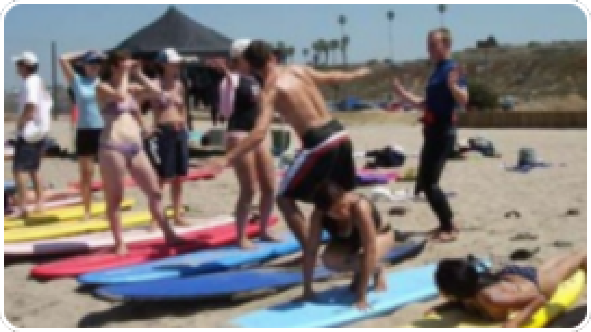 Group on beach practicing surfing on sand with surfboards.