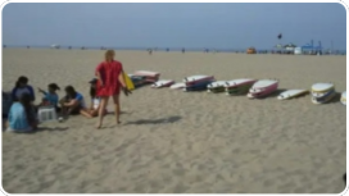Group on beach near stacked surfboards, with person in red standing.