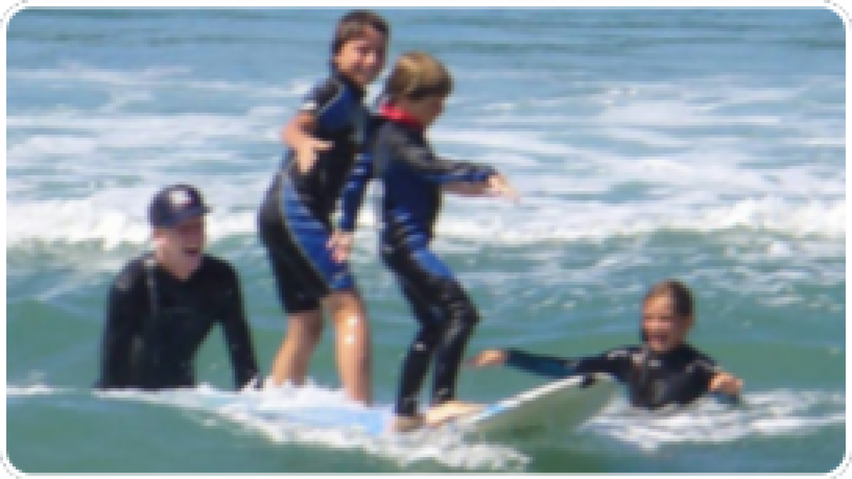 Four people surfing together on a surfboard in the ocean.