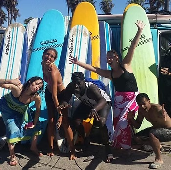 Group of people posing enthusiastically with surfboards in front of a van.